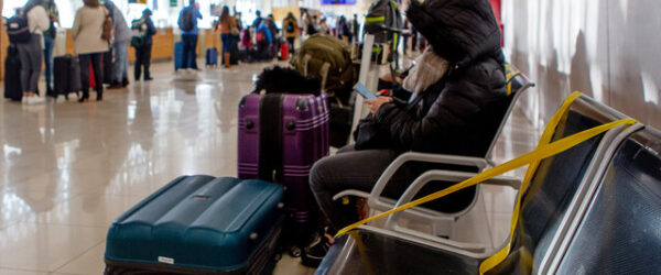 Una mujer con su equipaje de viaje, parca y capucha espera sentada en una banca del aeropuerto a que sea su turno para abordar el avión durante el primer día de fin de semana largo que se vive en el país