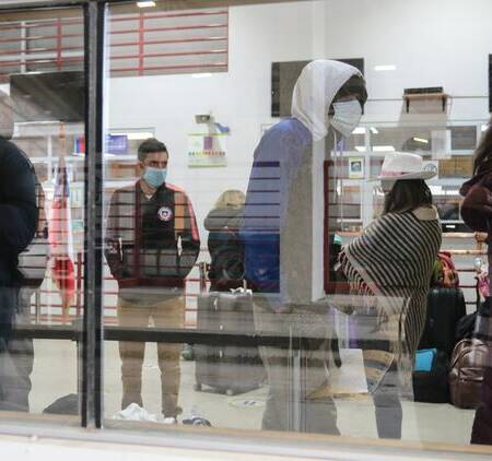 La imagen muestra a un grupo de migrantes detrás de un vidrio