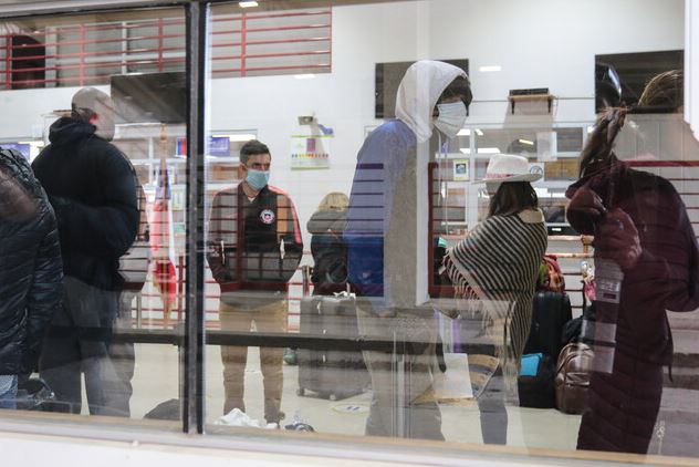 La imagen muestra a un grupo de migrantes detrás de un vidrio