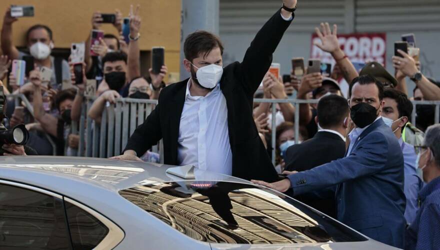 Gabriel Boric saliendo del auto presidencial y levantando la mano para saludar a la gente.