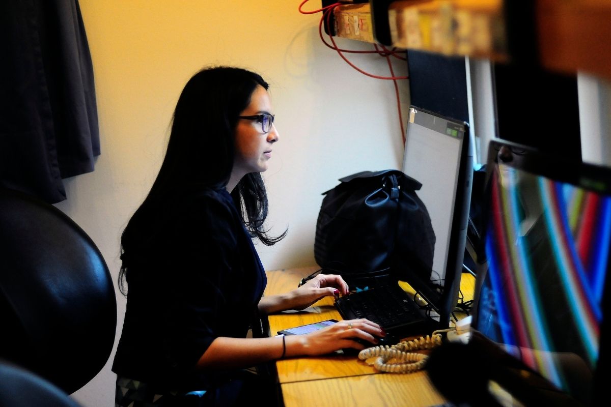 Una mujer vestida de negro trabaja sentada frente a su computador.