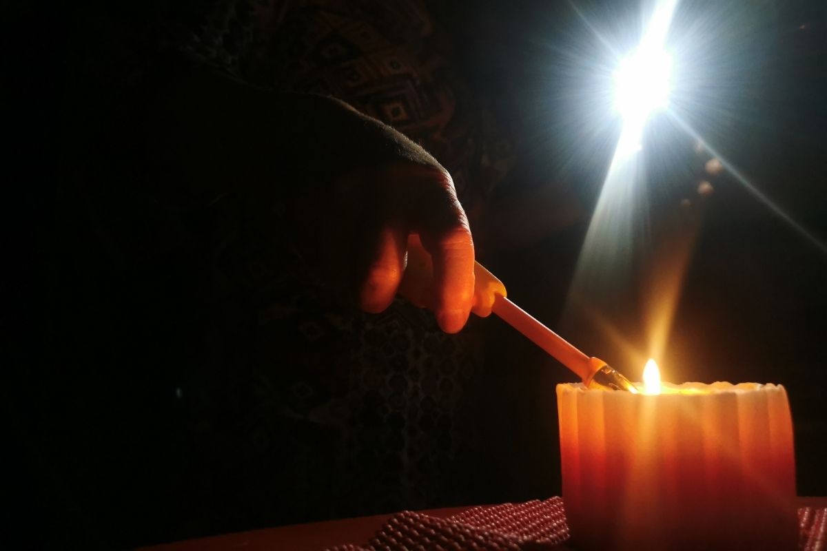 Una mano con un fósforo enciende una vela en medio de la penumbra causada por un corte de luz.