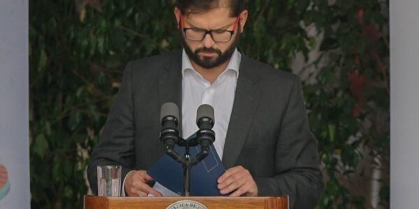 Gabriel Boric frente a un podio con el logo presidencial mirando hacia abajo como revisando unas carpetas que toma con sus manos