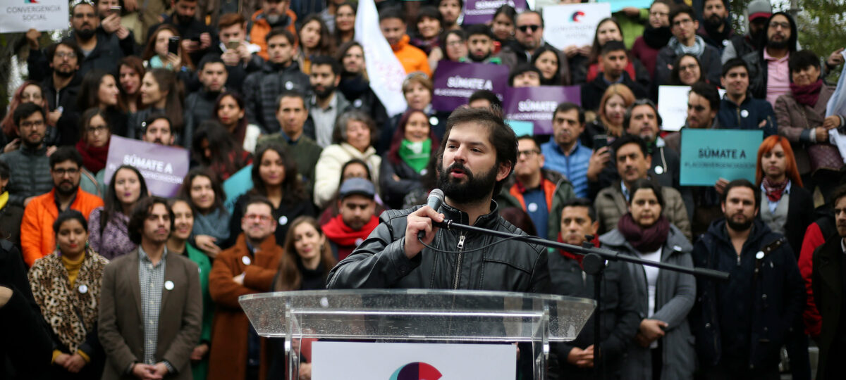 Gabriel Boric en un podio con un cartel de Convergencia Social y la militancia de ese partido detrás de él