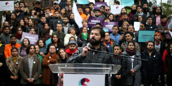 Gabriel Boric en un podio con un cartel de Convergencia Social y la militancia de ese partido detrás de él