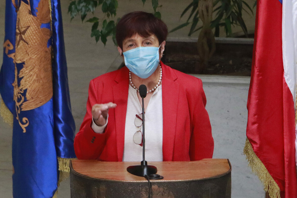 Carmen Hertz. Aarece tras un podio en la Cámara de Diputados, con su mano izquierda abajo y su mano derecha a media altura y haciendo una pinza con sus dedos índices y pulgar.