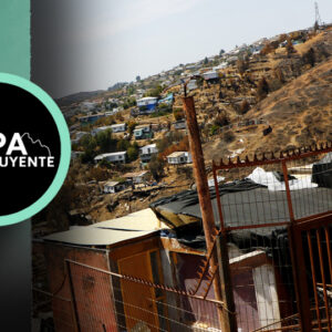Un campamento de Valparaíso se encumbra entre los cerros. En primer plano, una vivienda construida con materiales livianos y una bandera chilena izada.