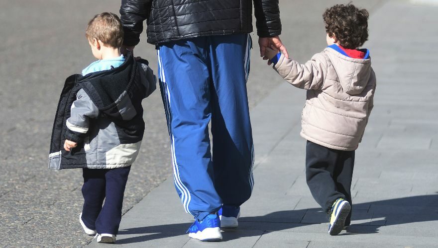 Un padre lleva de la mano a dos niños mientras se aleja de la cámara