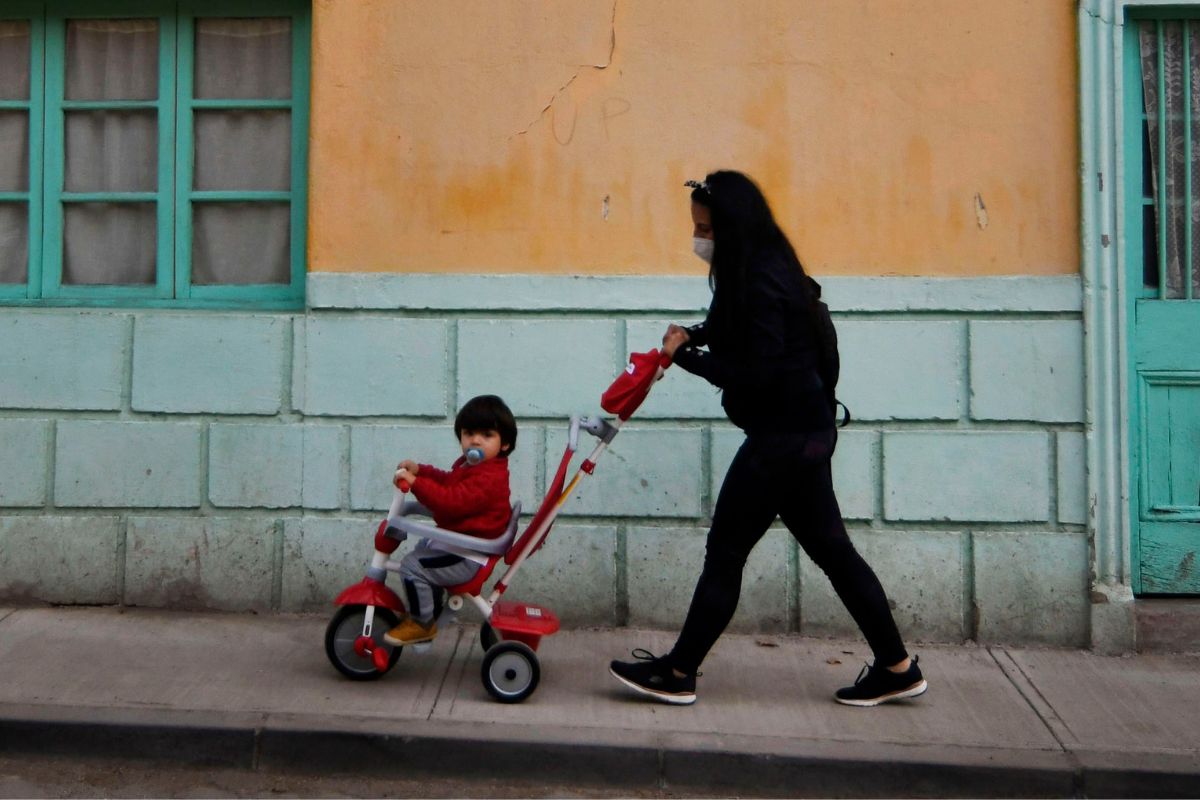 Una mujer lleva a su hijo en un triciclo guiado calle arriba.