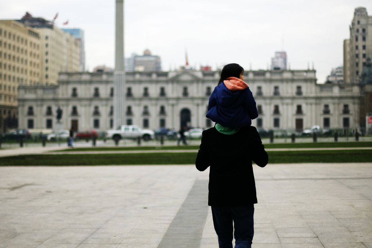 Un padre lleva en sus hombros a su hijo, mientras ambos miran el Palacio de La Moneda
