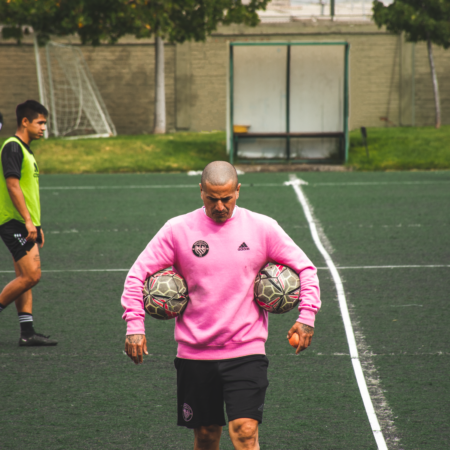 Jorge "Kike" Acuña, entrenador de Santiago City, con una pelota en cada brazo mientras dirige el entrenamiento del club que se prepara para enfrentar a Colo-Colo