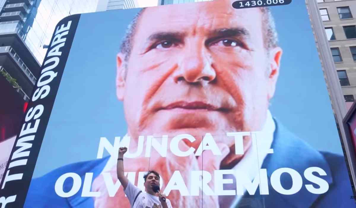 Fabrizio Copano posando junto a una pantalla donde está proyectada la foto de Checho Hirane en Times Square